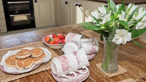 A kitchen counter with a bowl of strawberries, a vase with white flowers, and plates with pancakes.
