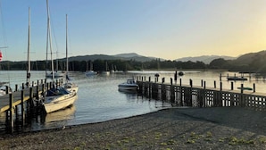 Un puerto deportivo con barcos amarrados, un muelle de madera y una masa de agua tranquila con colinas al fondo.