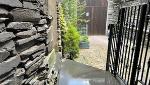 Un muro de piedra, una reja metálica y un camino empedrado que conduce a un edificio.