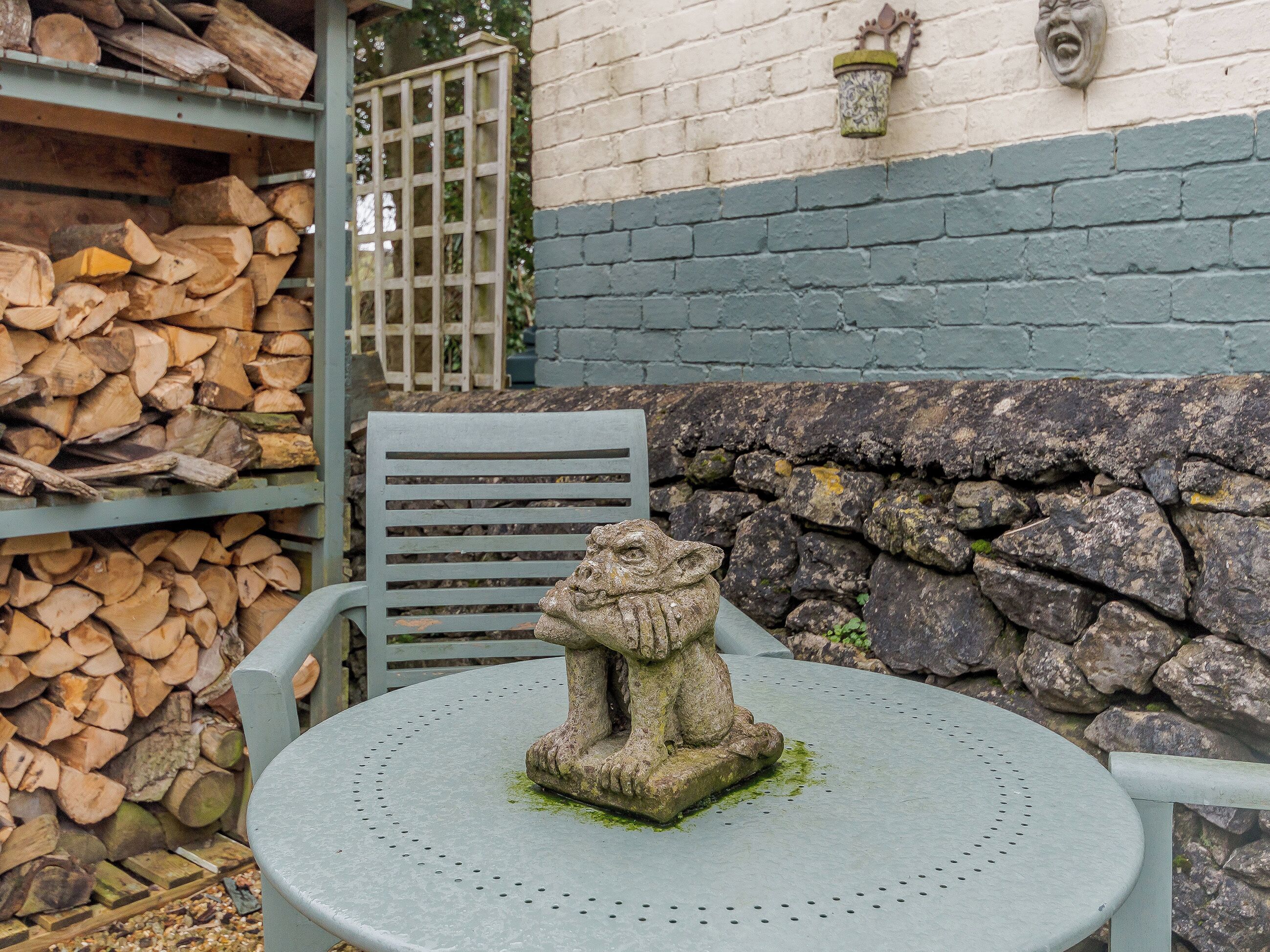 Una estatua de piedra sobre una mesa, una silla y un muro de piedra con una puerta al fondo.