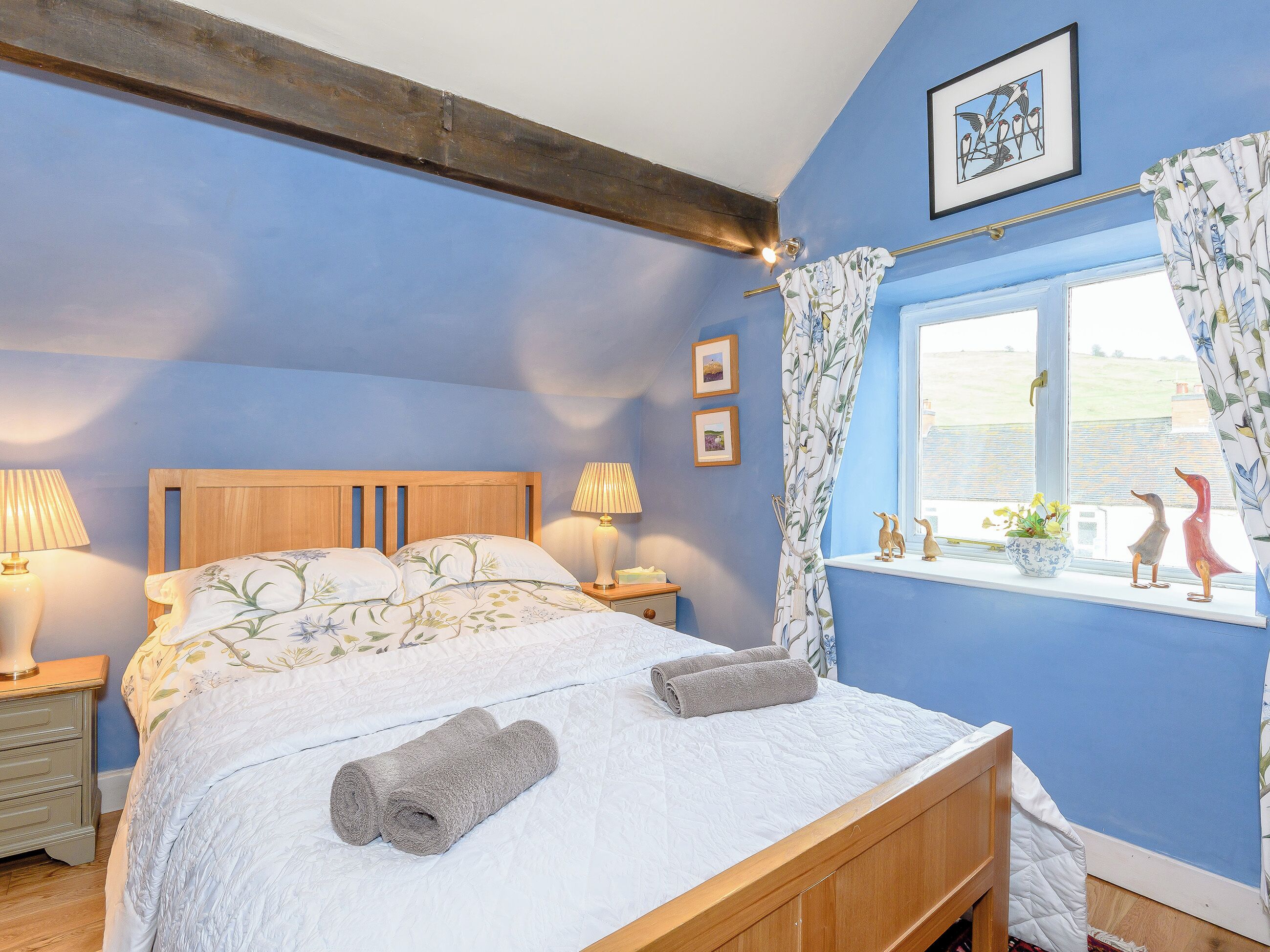 A bedroom with a wooden bed, two bedside lamps, a window with a view, and a blue wall.