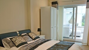 Une chambre à coucher comprenant un lit, une table de chevet, une armoire et une porte-fenêtre coulissante donnant sur un balcon.