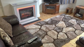 Un salon avec une cheminée, un téléviseur posé sur un meuble en bois, un canapé en cuir marron et un tapis à motifs de pierre.