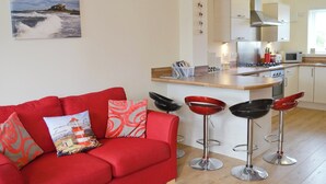 Een moderne woonkamer met een rode bank, een keuken met witte kasten en een eethoek met rode barstoelen.