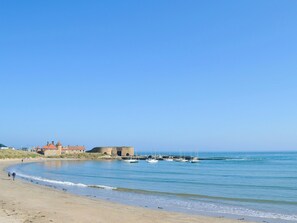 Ein Strand mit sandigem Ufer, einer Steinfestung und mehreren Booten, die am Wasser liegen.