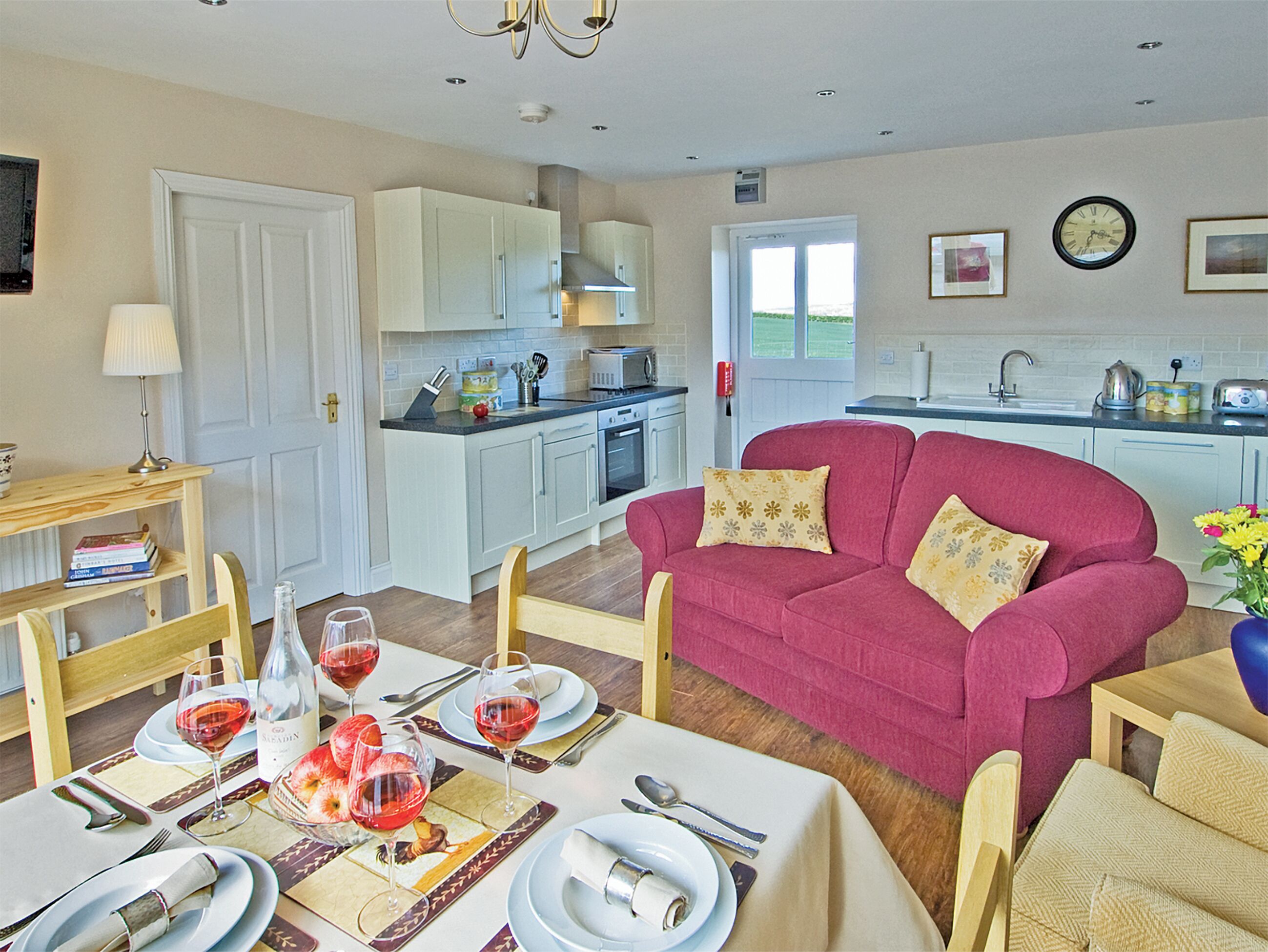 A modern kitchen with white cabinets, a dining area with a pink sofa, and a table set for a meal.