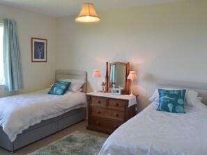 A bedroom with two beds, a dresser, a mirror, and a hanging light fixture. - 3 bedroom accommodation in Church Bay, Anglesey (Church Bay, Anglesey)