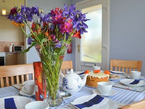 A dining table with a vase of flowers, a teapot, and a cake. - 3 bedroom accommodation in Church Bay, Anglesey (Church Bay, Anglesey)