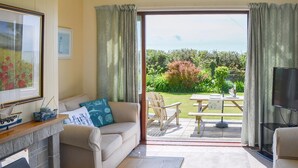 Ein Wohnzimmer mit einer Couch, einem Couchtisch, einem Kamin und Blick auf einen Garten durch eine Schiebetür.