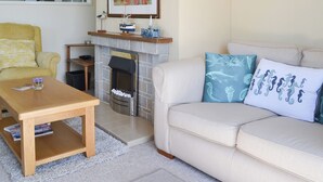 Ein Wohnzimmer mit Kamin, einem gelben Sessel, einem beigen Sofa mit blauen Kissen und einem gerahmten Bild über dem Kamin.