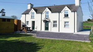 A two-story house with a front porch, a chimney, and a gravel driveway. - 3 bedroom accommodation in Llaneilian, near Amlwch (Llaneilian, near Amlwch)