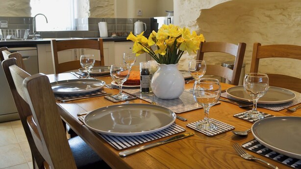 A dining table set with plates, cutlery, and glasses, with a vase of yellow flowers in the center. - 3 bedroom accommodation in Llaneilian, near Amlwch (Llaneilian, near Amlwch)