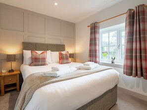 A neatly made bed with white linens and plaid pillows, a bedside lamp, and a window with plaid curtains. - 4 bedroom accommodation in Cayton, near Scarborough (Cayton, near Scarborough)