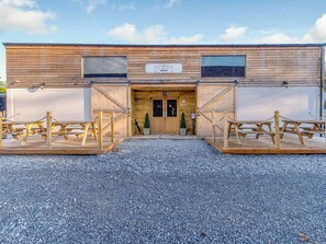 Un edificio de estilo granero de madera con un camino de grava y mesas de picnic.