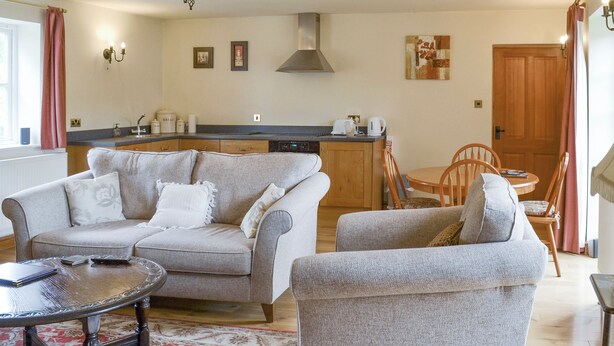 A living room with a sofa, armchair, and coffee table, a dining area with a table and chairs, and a kitchen with a stove and cabinets. - 1 bedroom accommodation in Cropton, near Pickering (Cropton, near Pickering)