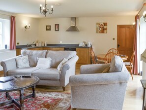 Ein Wohnzimmer mit Sofa, Sessel und Couchtisch, ein Essbereich mit Tisch und Stühlen sowie eine Küche mit Herd und Schränken.