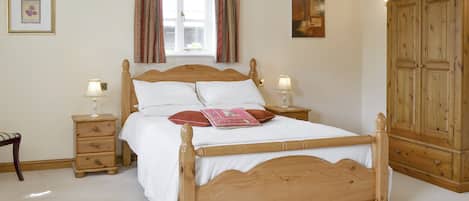 A bedroom with a wooden bed, two bedside tables with lamps, a wardrobe, and a window with curtains.