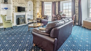 A living room with a sofa, armchairs, a TV, a fireplace, and patterned wallpaper. - 2 bedroom accommodation in Ilfracombe (Ilfracombe)