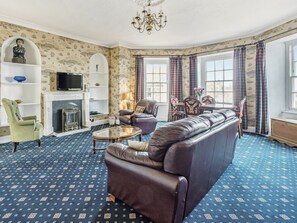 A living room with a sofa, armchairs, a TV, a fireplace, and patterned wallpaper.