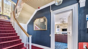 A staircase with red carpeted steps and white railings, a blue wall with a star-patterned ceiling, and a doorway leading to a room with patterned flooring. - 2 bedroom accommodation in Ilfracombe (Ilfracombe)