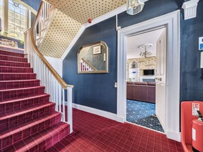 A staircase with red carpeted steps and white railings, a blue wall with a star-patterned ceiling, and a doorway leading to a room with patterned flooring.