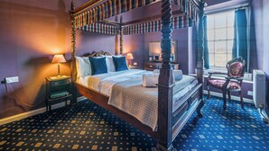 A four-poster bed with a canopy, a nightstand with a lamp, a chair, and a window with curtains. - 2 bedroom accommodation in Ilfracombe (Ilfracombe)