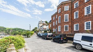 A street with parked cars and a brick building with multiple windows. - 2 bedroom accommodation in Ilfracombe (Ilfracombe)