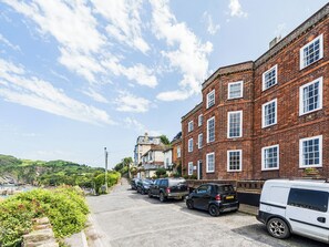 A street with parked cars and a brick building with multiple windows. - 2 bedroom accommodation in Ilfracombe (Ilfracombe)