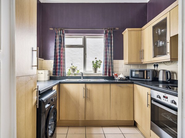 A compact kitchen with wooden cabinets, a washing machine, a microwave, and an oven.
