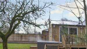 Una vasca idromassaggio su un pontile di legno, con una recinzione in legno e un albero sullo sfondo.