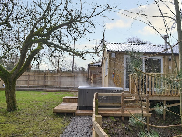 Un bain à remous sur une terrasse en bois, avec une clôture en bois et un arbre en arrière-plan.