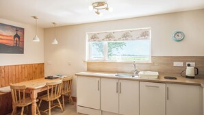 Une cuisine avec une table et des chaises en bois, une fenêtre donnant sur un beau paysage et une horloge au mur.