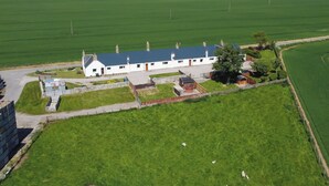 Un bâtiment blanc surmonté d’un toit bleu, entouré de champs verdoyants et avec une étendue d’eau en arrière-plan.
