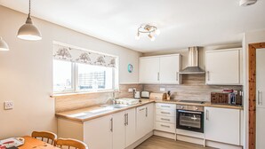 Une cuisine moderne avec des armoires blanches, un plan de travail en bois, un four encastré et une fenêtre donnant sur un chantier de construction.