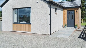 A small, single-story building with a sloped roof, a large window, and a wooden door. - 1 bedroom accommodation in Newton, near Tain (Newton, near Tain)
