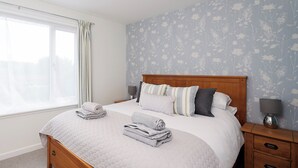 A neatly made bed with a quilted cover, a wooden headboard, and a nightstand with a lamp. - 1 bedroom accommodation in Newton, near Tain (Newton, near Tain)
