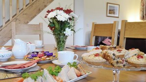 A table set with sandwiches, pastries, a pitcher, cups, and a vase of flowers.