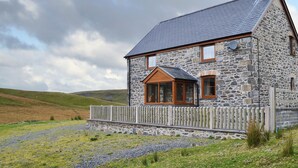 A stone house with a sloped roof, wooden windows, and a wooden fence.