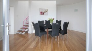 Un coin repas avec un plancher en bois, une table entourée de chaises, un vase rempli de fleurs et un escalier doté d’une rampe rose.