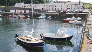 Un port où plusieurs bateaux sont amarrés, un bâtiment sur lequel on peut lire l’inscription « DUNURE INN », et un mur de pierre en arrière-plan.