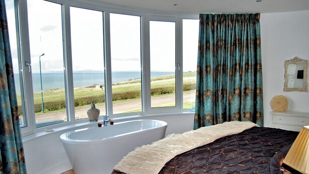 Une chambre avec une grande fenêtre, une baignoire et un lit recouvert d’une couvre-lit à motifs.