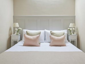 A neatly made bed with two pillows, a bedside table with a lamp and a vase of flowers, and a wall with a panel design. - 3 bedroom accommodation in Pickering (Pickering)