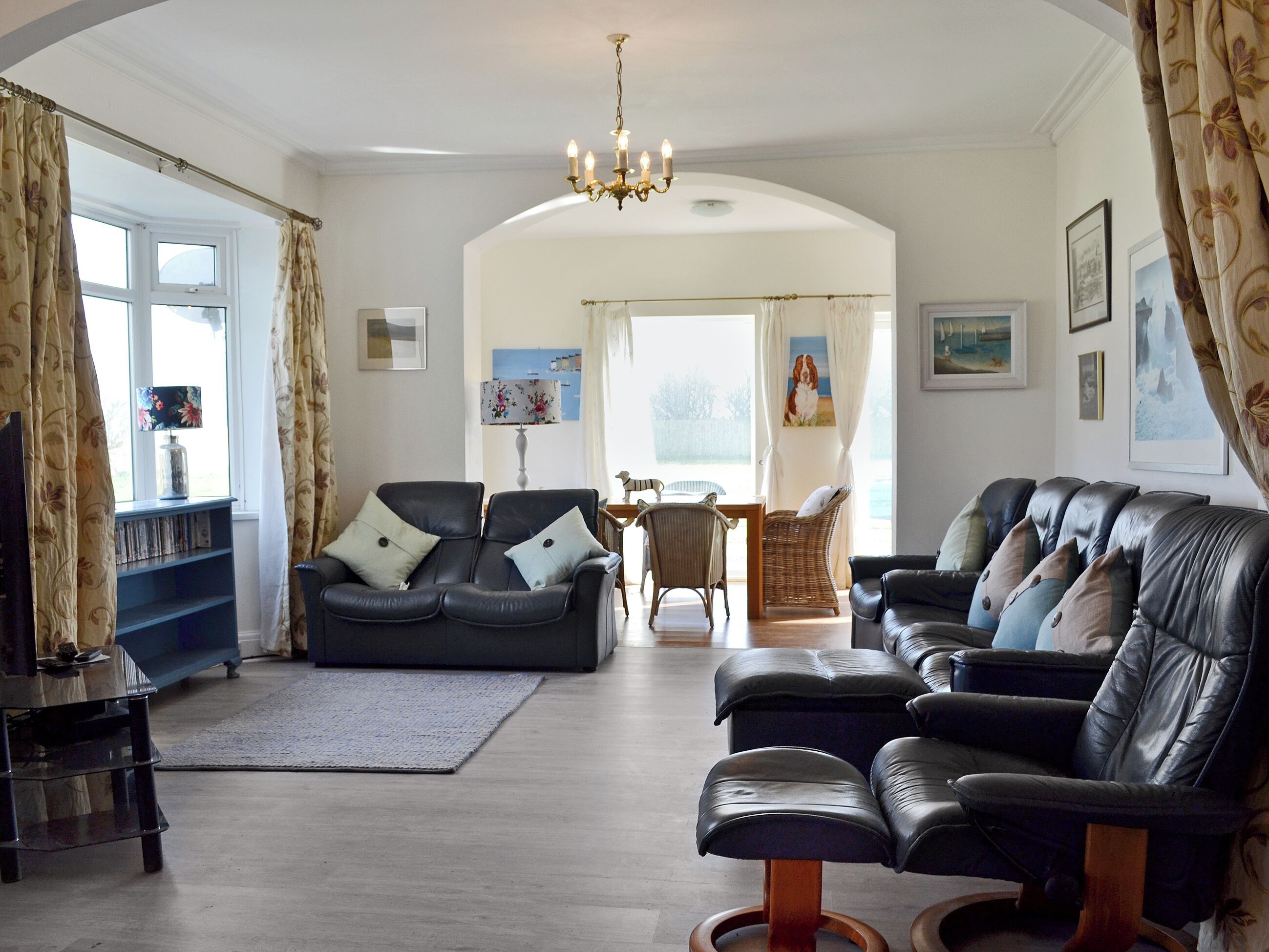 Een woonkamer met een zwarte leren bank, een eettafel met stoelen en een kroonluchter.