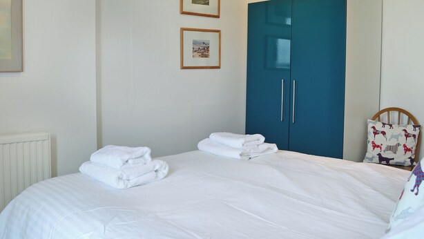 A bedroom with a bed, white linens, a blue wardrobe, and two framed pictures on the wall.