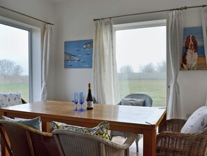 Un comedor con mesa de madera, sillas de mimbre y vistas al campo a través de amplios ventanales.