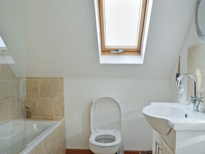 Un baño con tragaluz, inodoro, lavamanos y bañera.