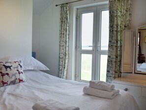 Habitación de hotel con cama, ropa de cama blanca, par de toallas, espejo y ventana con cortinas.