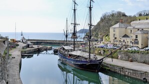 A historic sailing ship docked at a harbor with a building and a road nearby.