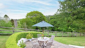 An outdoor patio with a table and chairs, surrounded by neatly trimmed hedges and a wooden fence.