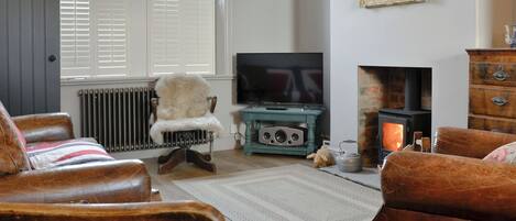 A living room with a fireplace, a television, and a large window with shutters.